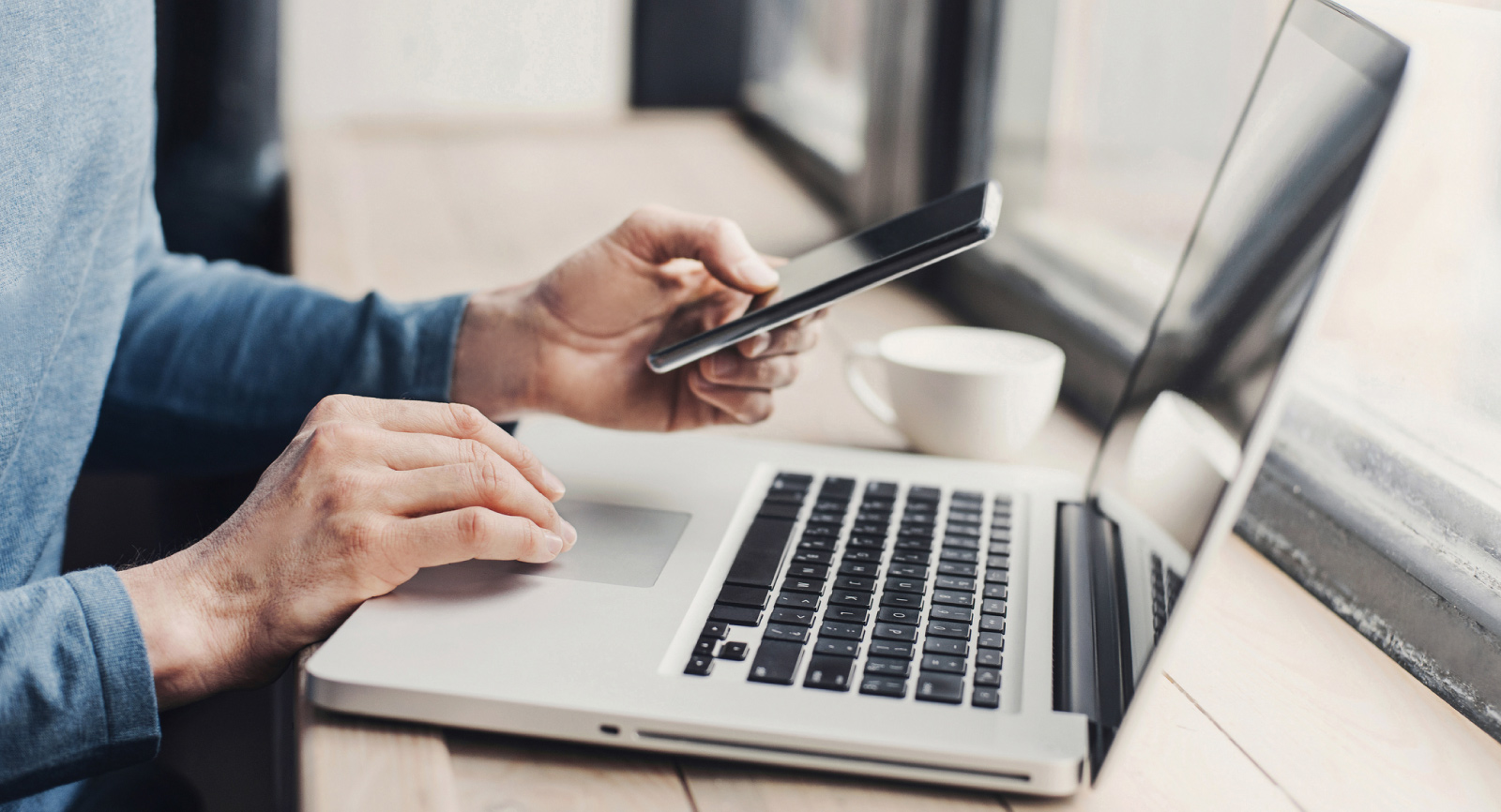 Person using a mobile phone and laptop computer at a coffee shop